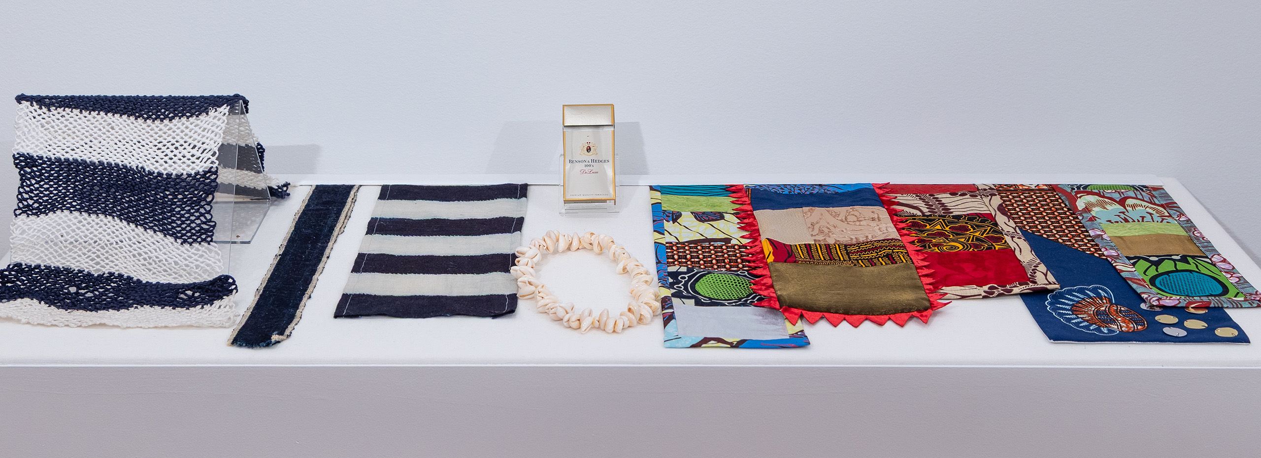 A white table displays samples of textiles, shells, and a cigarette box