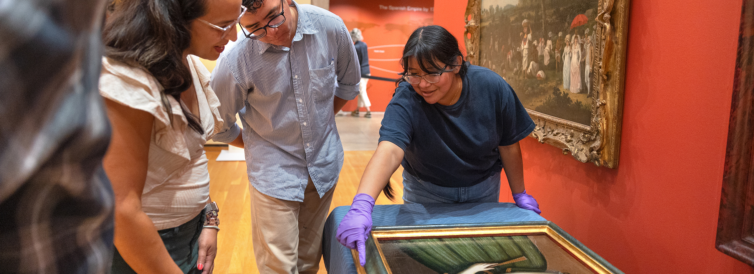 Students and an instructor look at a painting before it is hung on a museum wall