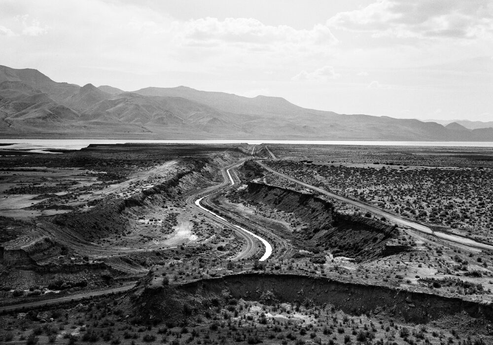 Black and white photograph of the Truckee Canal waterway with a mountain range in the background