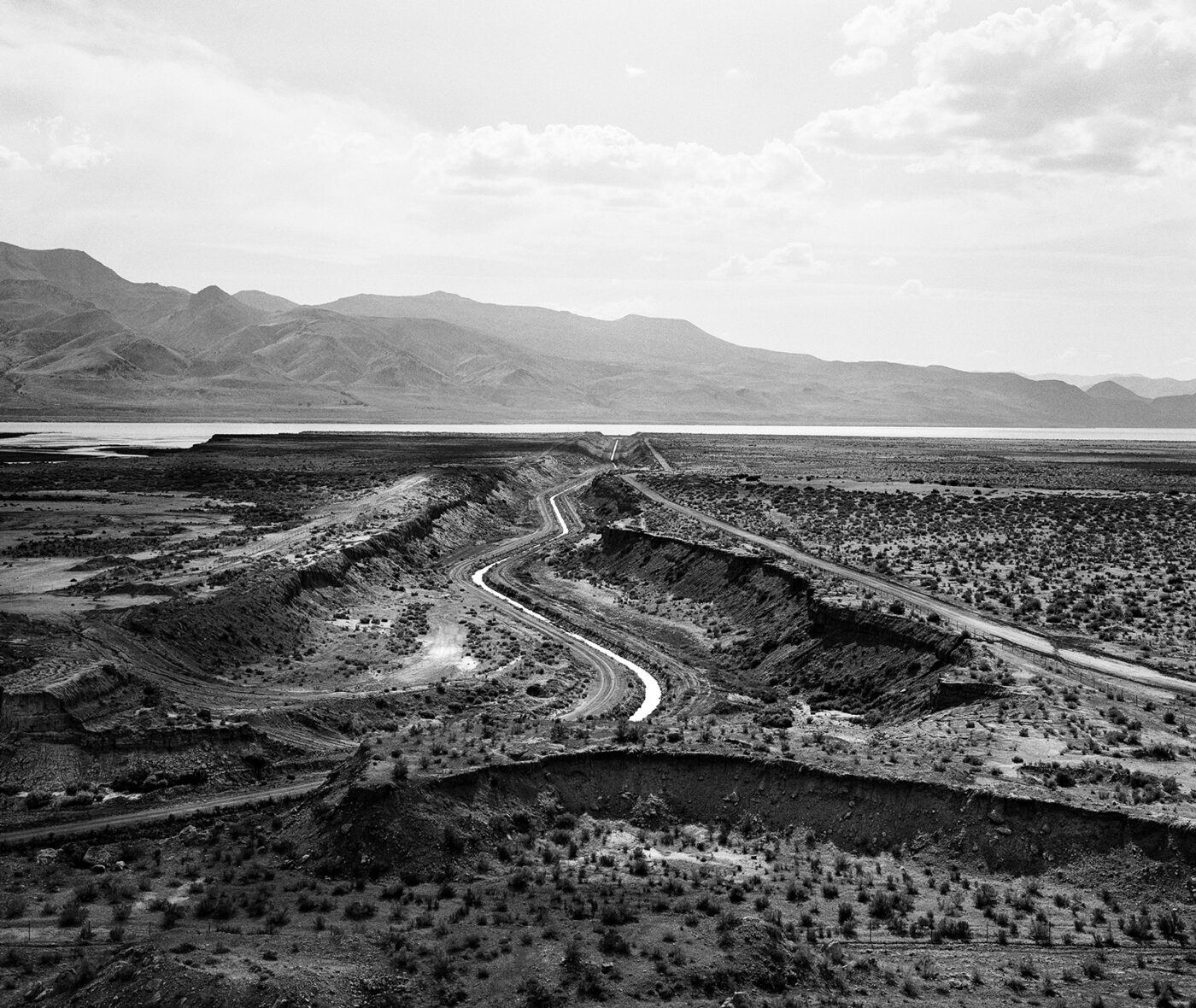 Black and white photograph of the Truckee Canal waterway with a mountain range in the background