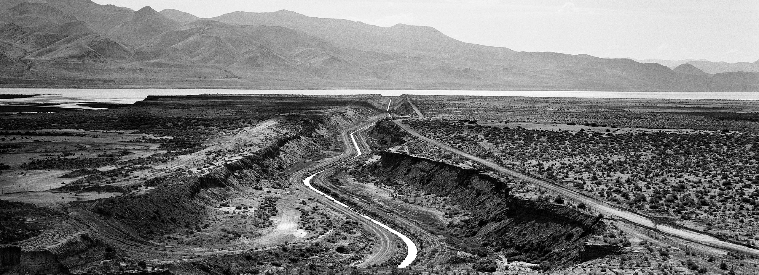 Black and white photograph of the Truckee Canal waterway with a mountain range in the background