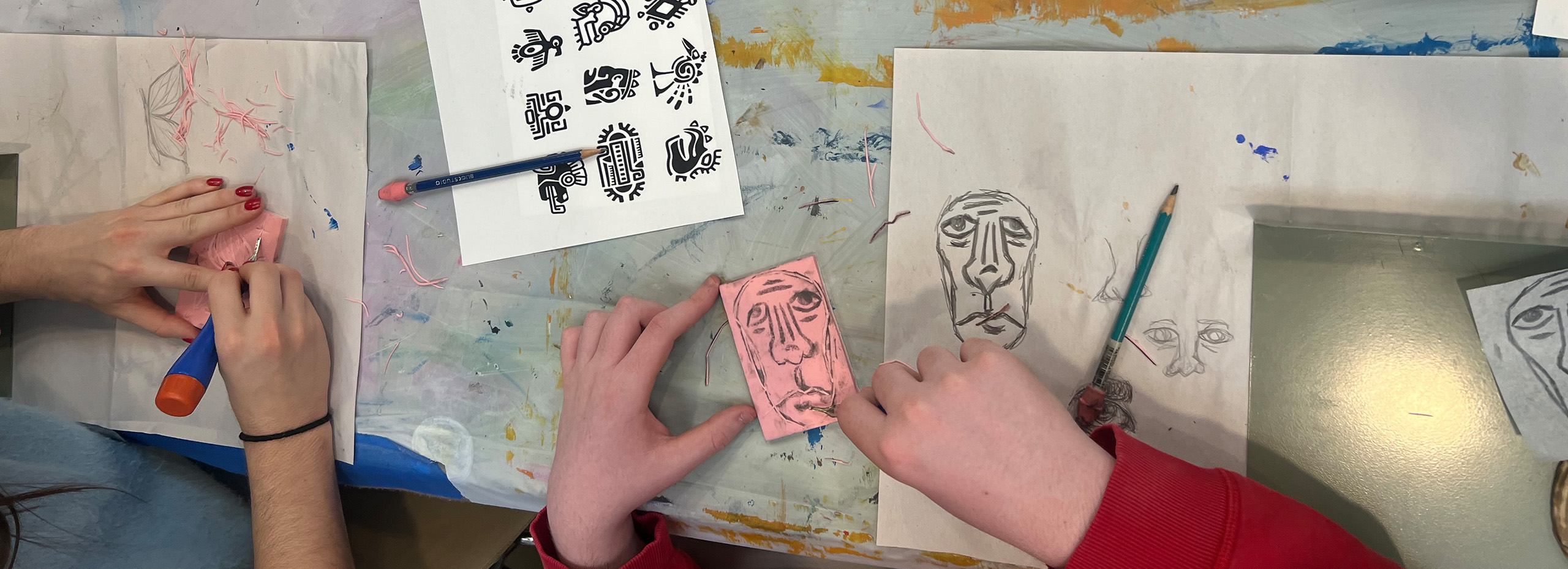 Hands sketch faces with pencil on a craft table with ancient stamps in black ink