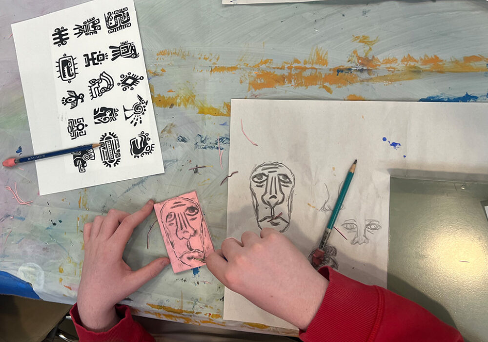 Hands sketch faces with pencil on a craft table with ancient stamps in black ink