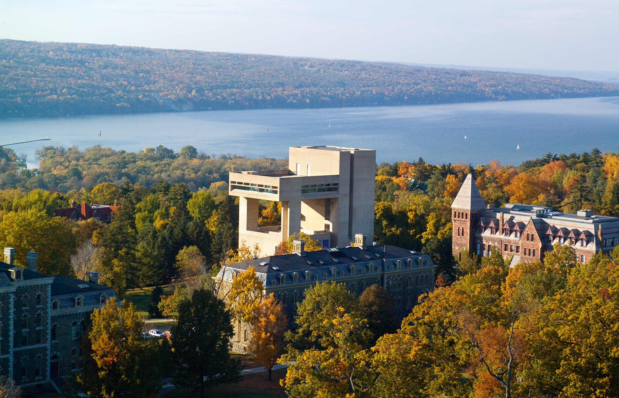Landscape showing a modern building surrounded by trees, classical buildings, and a lake with sailboats