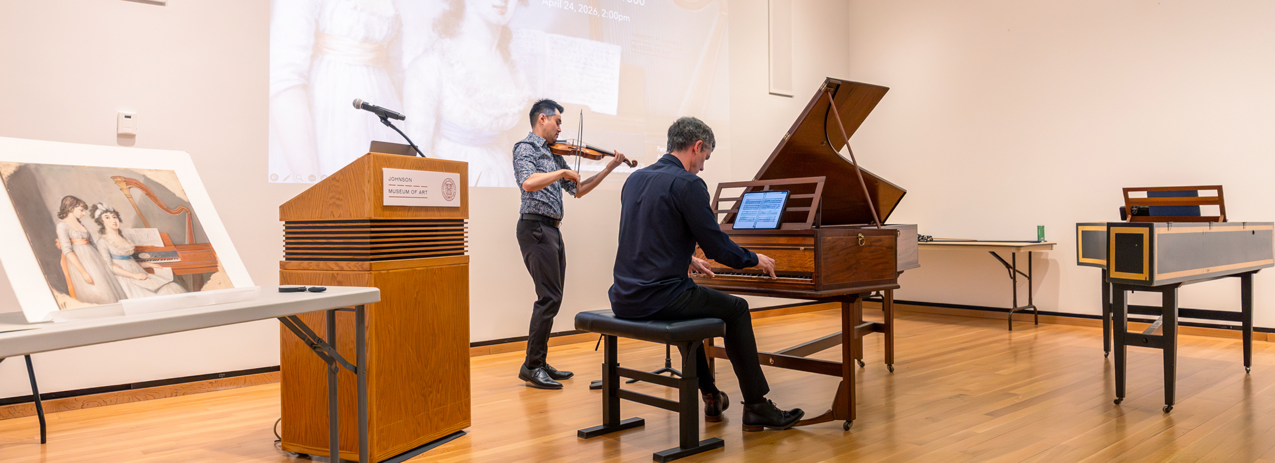 A piano and violin performance in front of a screen and an artwork displayed nearby