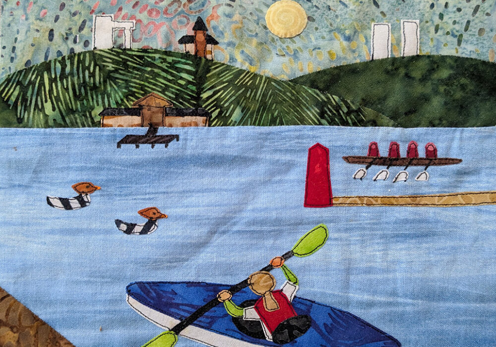 A quilted rendering of buildings on a hill and boats on a lake