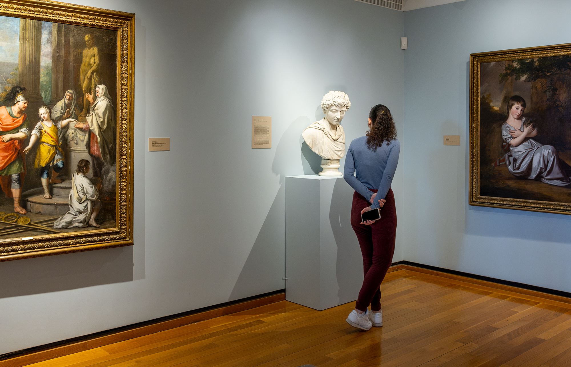 A woman looks at sculpture and paintings in a museum gallery