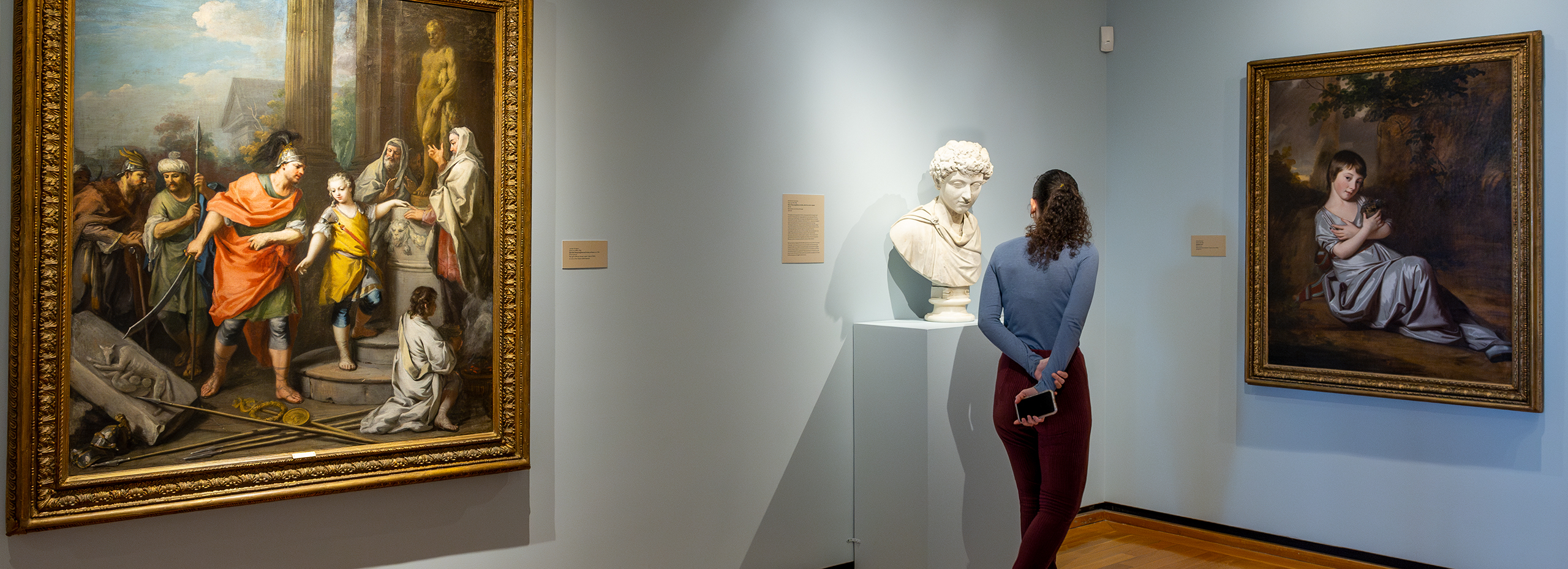 A woman looks at sculpture and paintings in a museum gallery