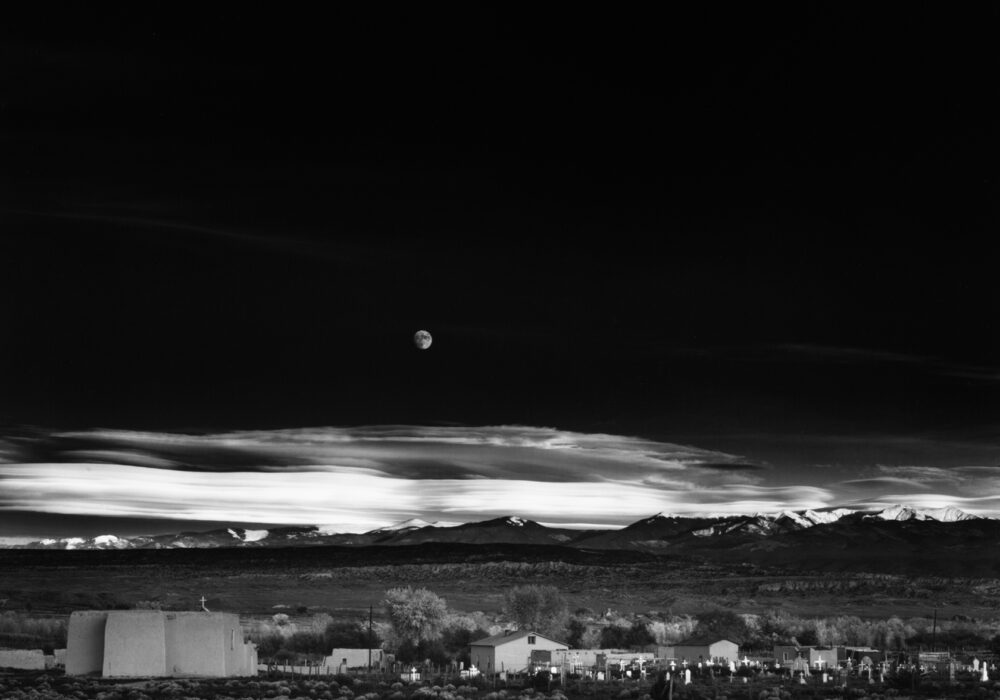 Black-and-white photograph of a moonrise over a village in New Mexico