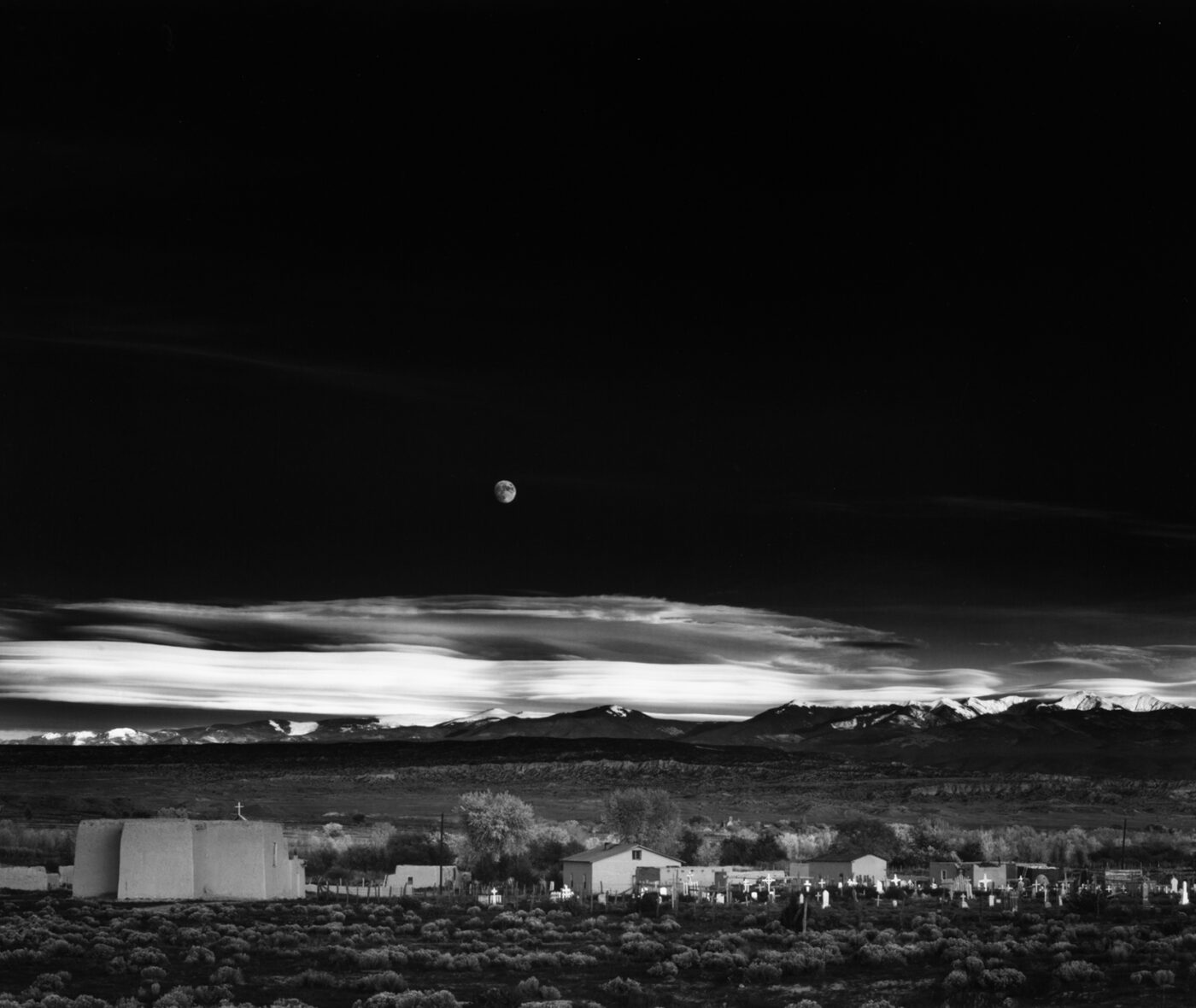 Black-and-white photograph of a moonrise over a village in New Mexico