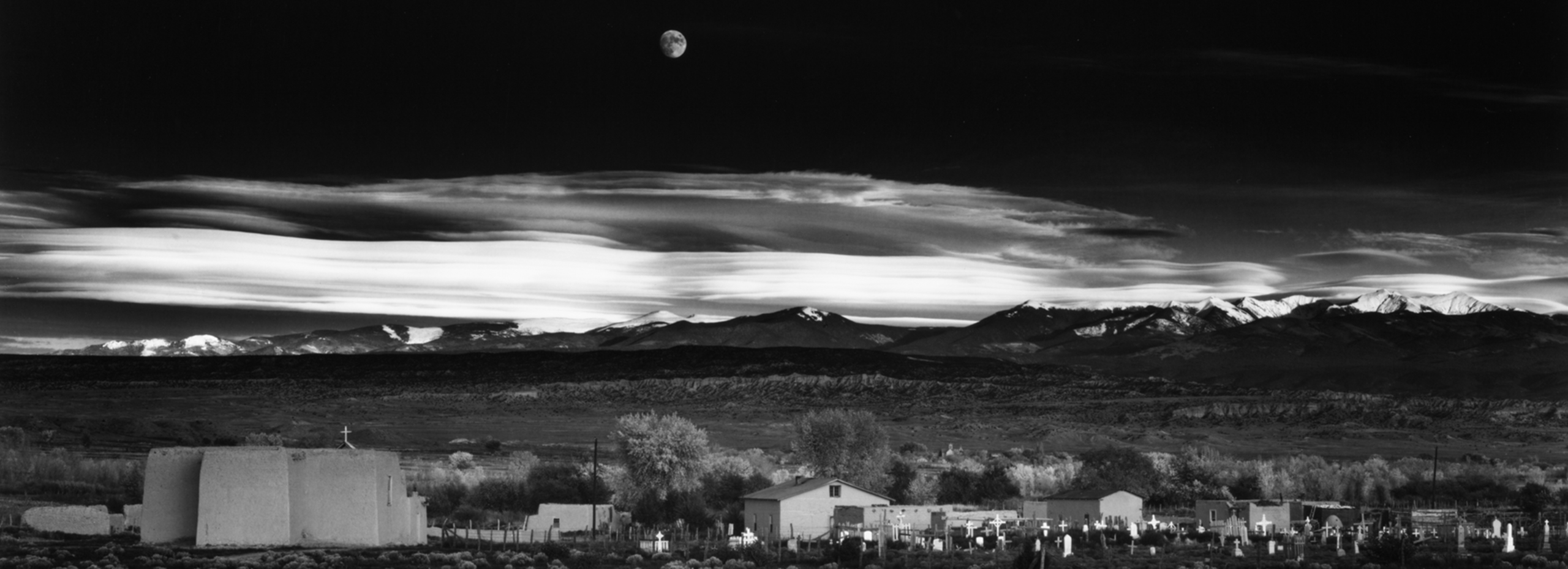 Black-and-white photograph of a moonrise over a village in New Mexico