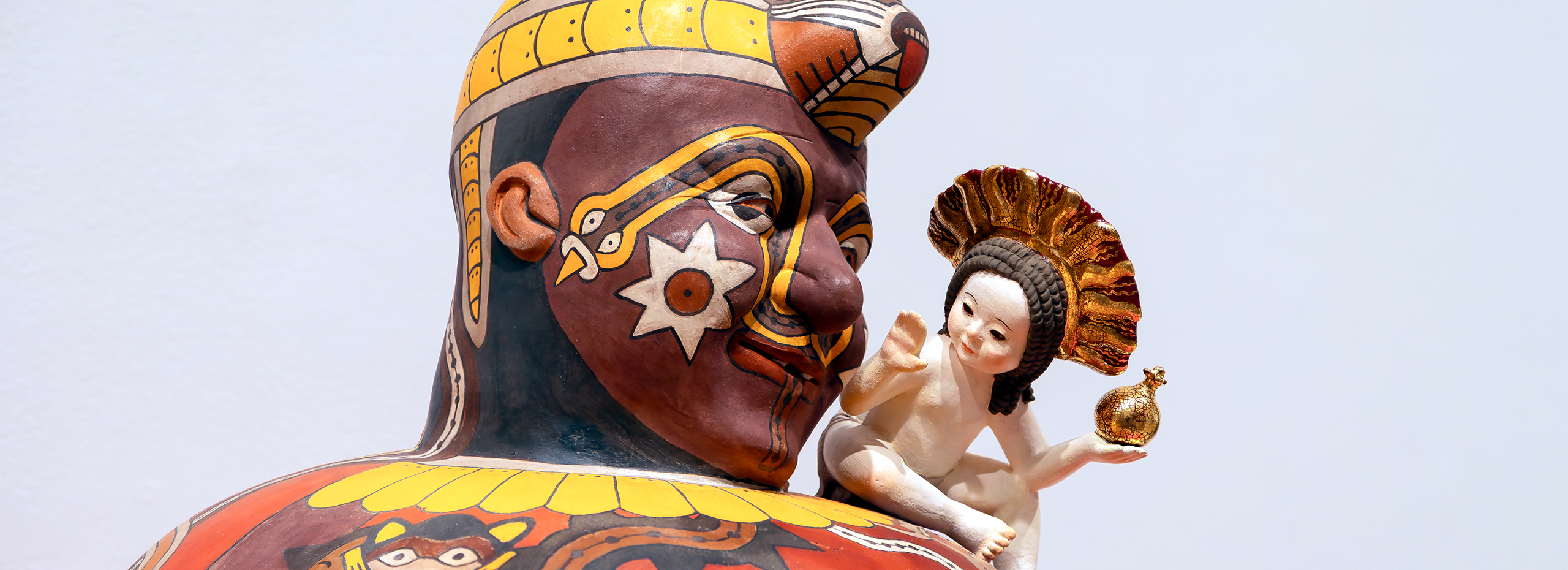 Closeup of the decorated face of a painted figurative sculpture with a tiny cherub on its shoulder