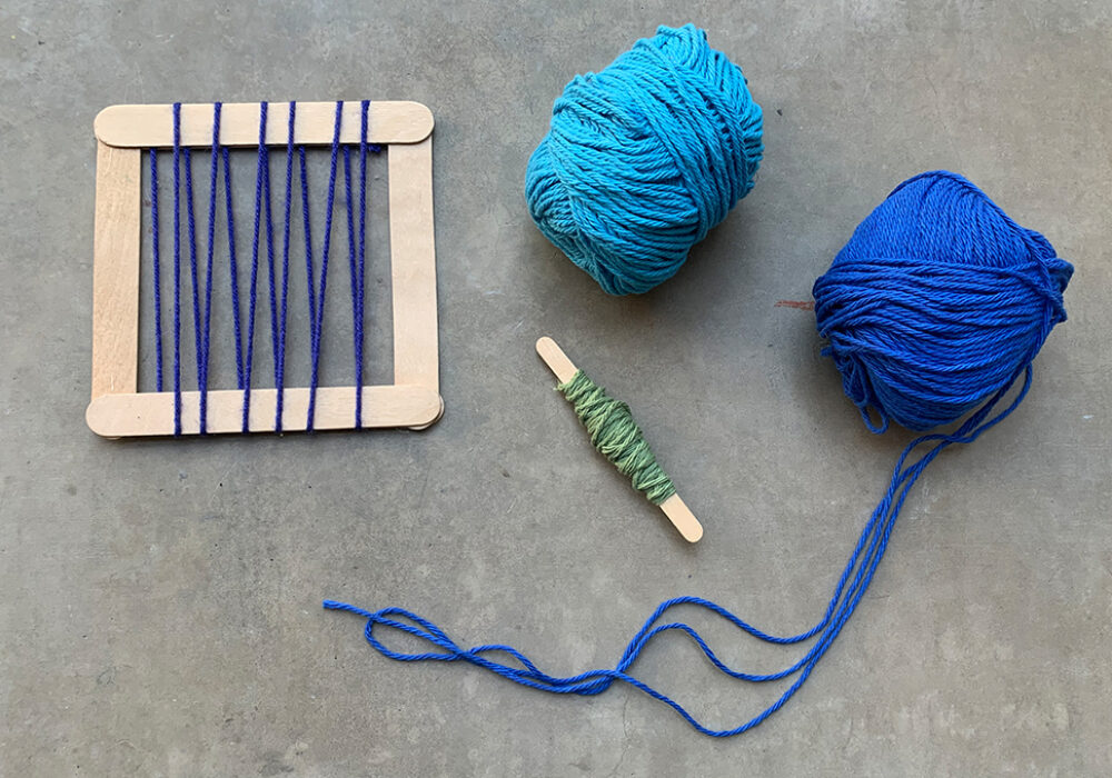 Tools for weaving including blue yarns, a spindle, and a popsicle-stick loom