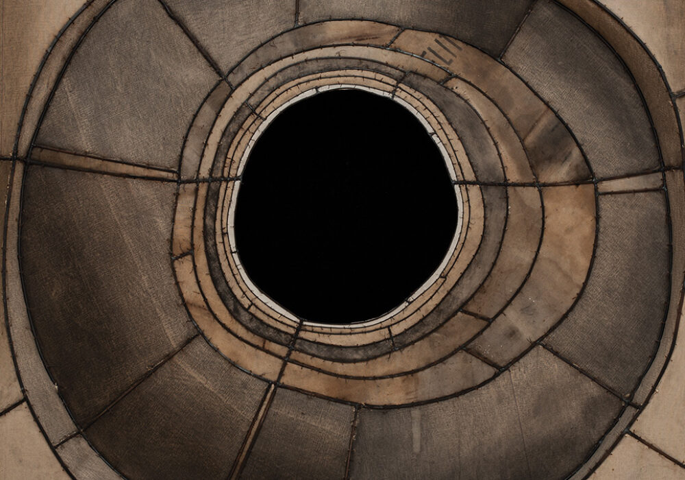 Portion of a hanging sculpture made of stitched brown canvas with a black hole at the center