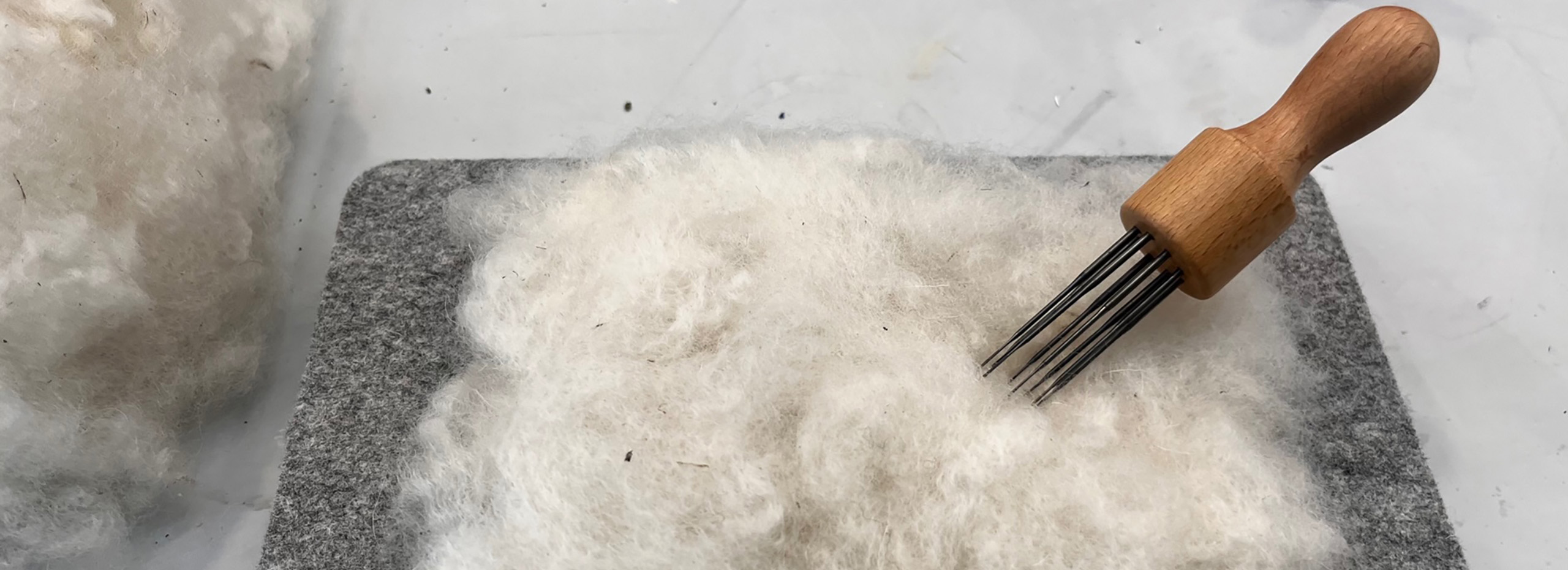 White wool, a needle tool, and a felt block for crafting