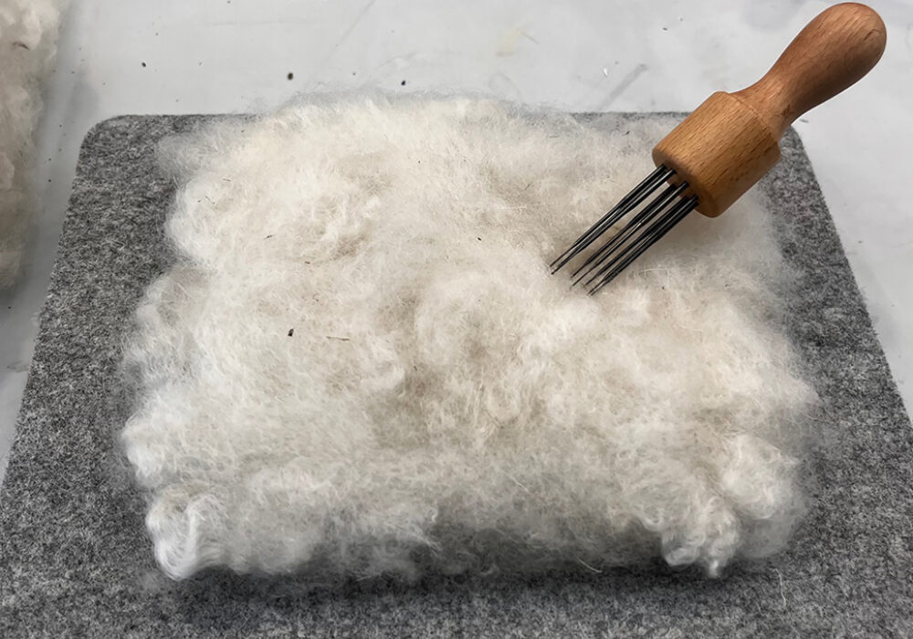 White wool, a needle tool, and a felt block for crafting