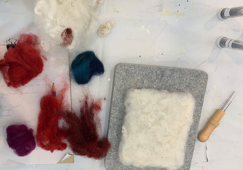 Piles of colorful wool, needle tools, and a felt block for crafting