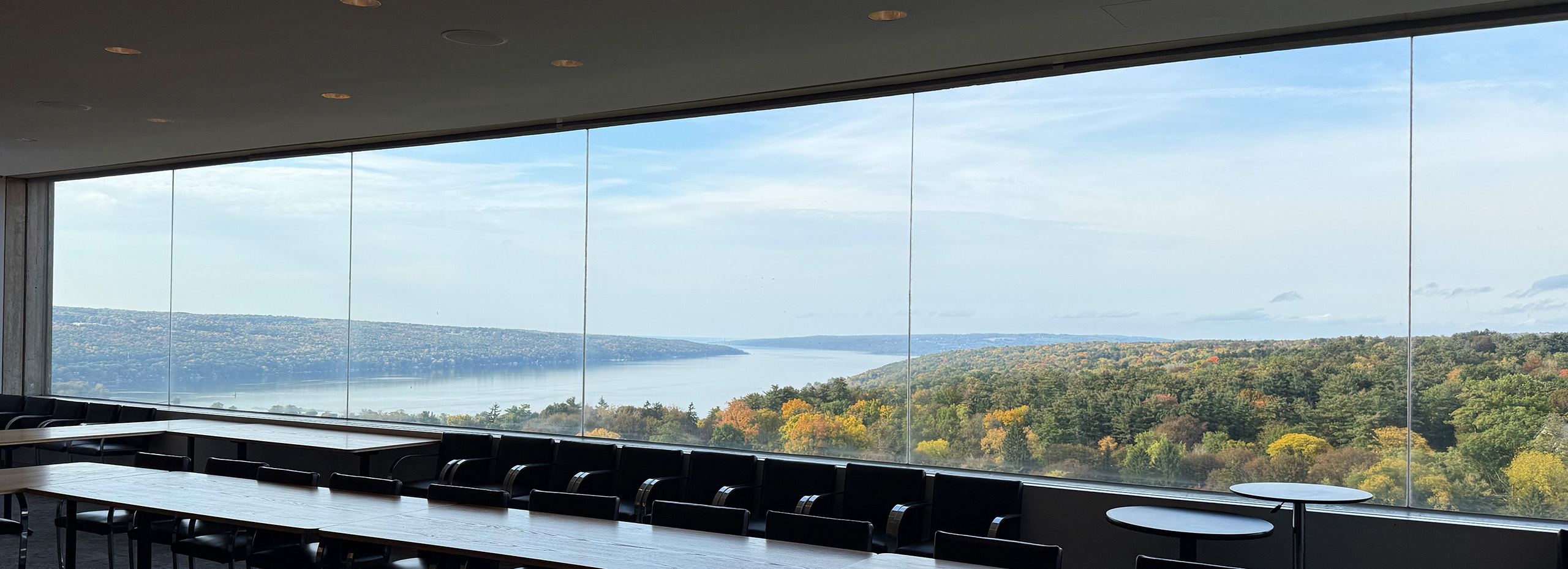 View of a lake and trees through the windows of a conference room with tables and chairs
