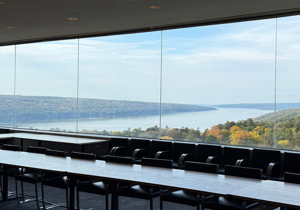 View of a lake and trees through the windows of a conference room with tables and chairs
